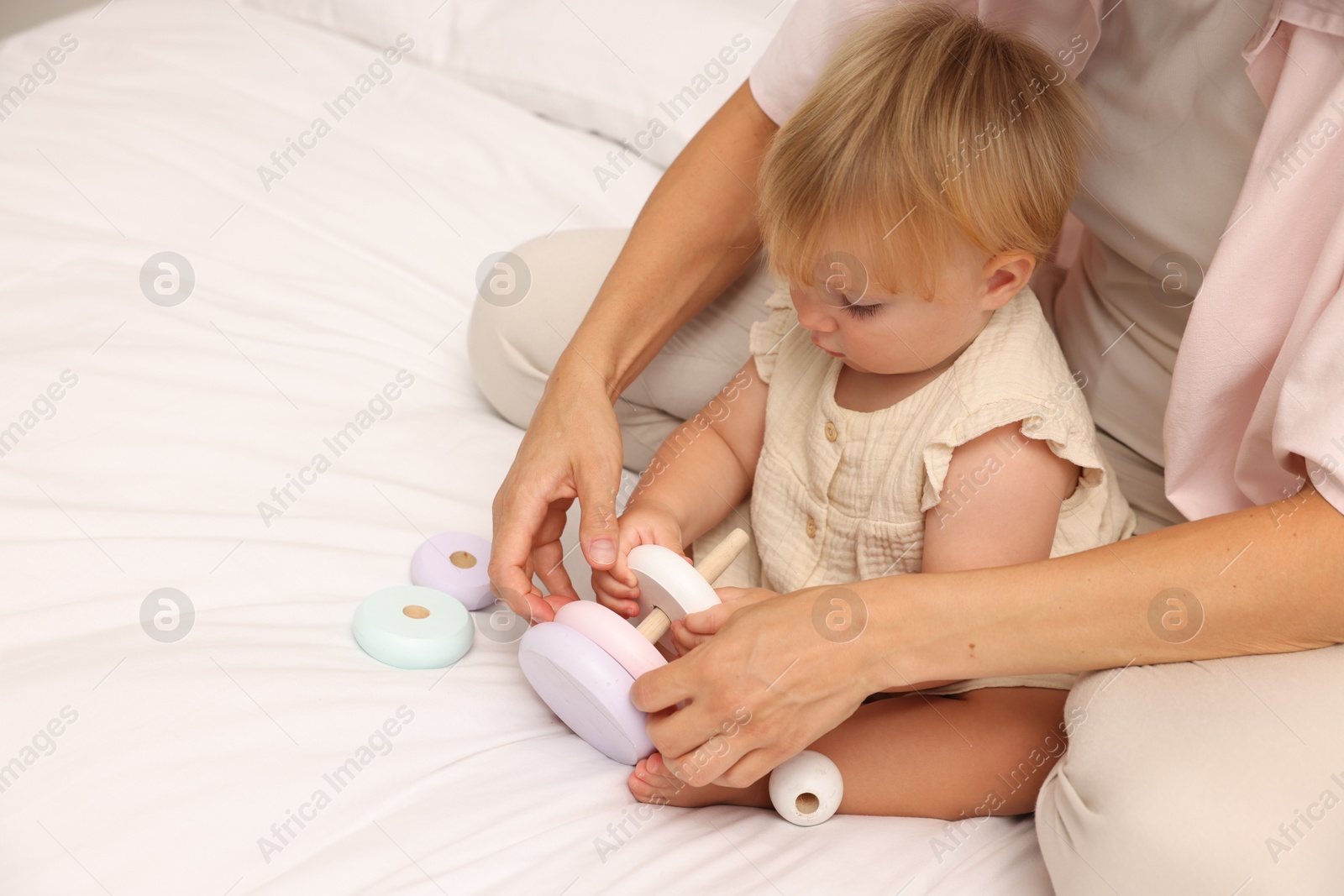 Cute baby girl and her mother playing with toy on bed at home, closeup. Space for text Photo of Cute baby girl and her mother playing with toy on bed at home, closeup. Space for text