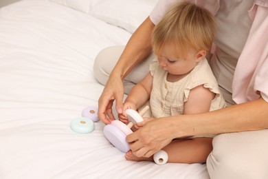 Photo of Cute baby girl and her mother playing with toy on bed at home, closeup. Space for text