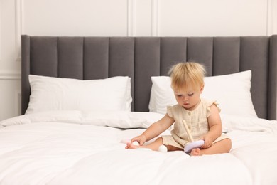 Photo of Cute baby girl playing with toy on bed at home. Space for text