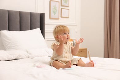 Photo of Cute baby girl in dress playing on bed at home