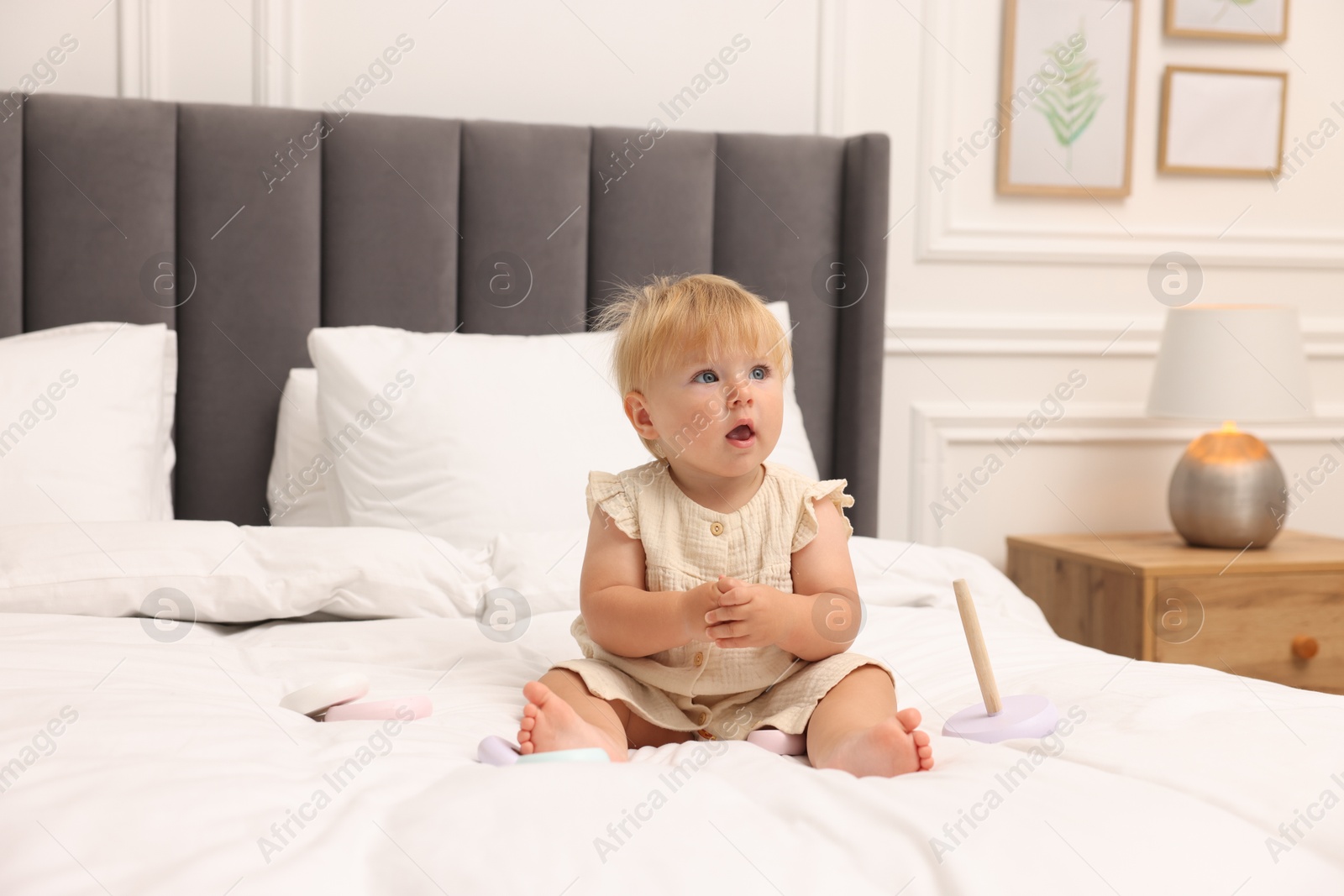 Cute baby girl in dress playing on bed at home Photo of Cute baby girl in dress playing on bed at home