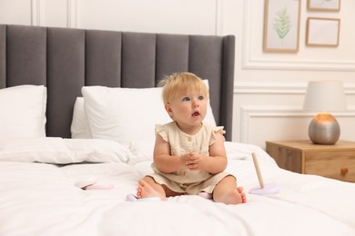 Photo of Cute baby girl in dress playing on bed at home