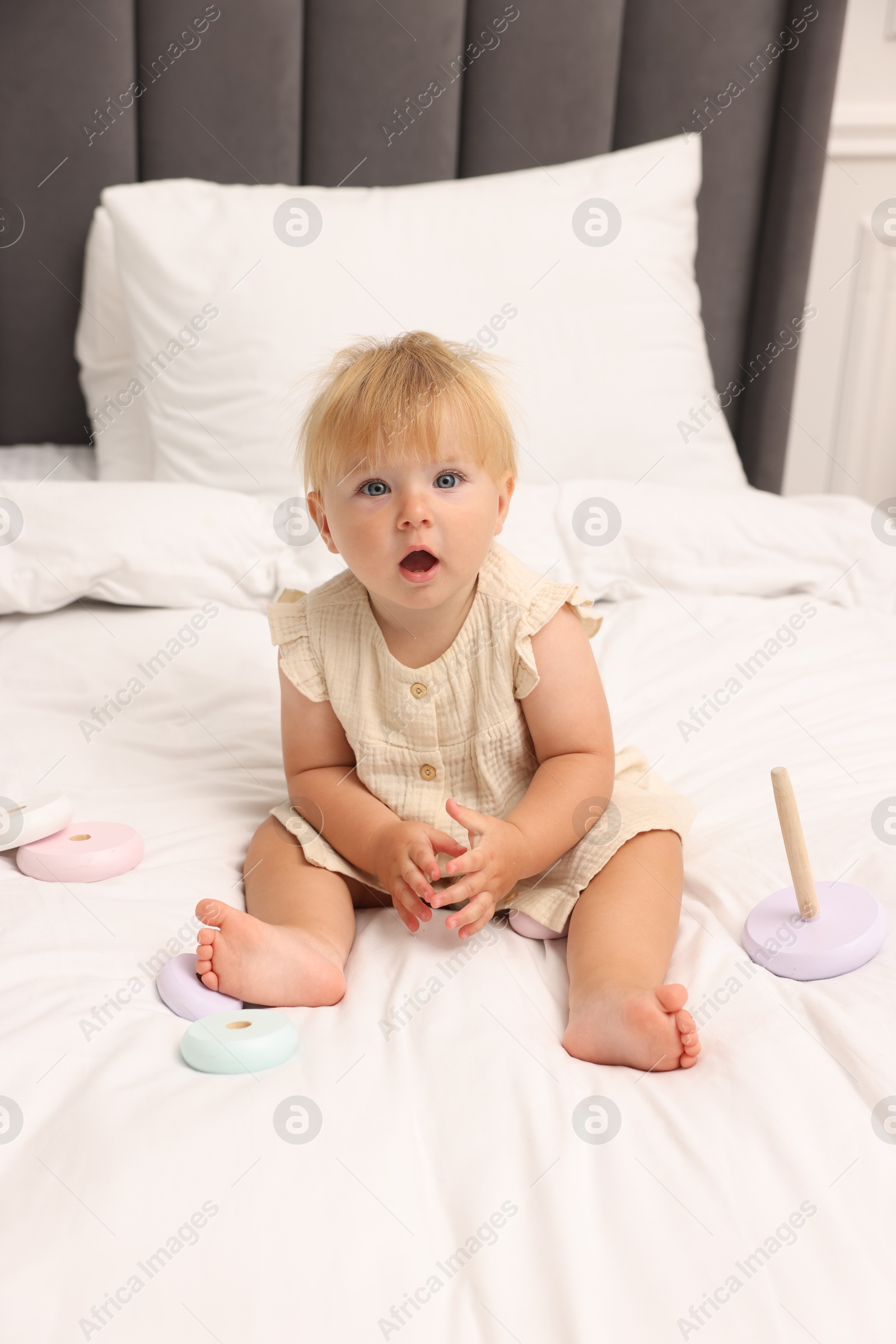 Cute baby girl in dress playing on bed at home Photo of Cute baby girl in dress playing on bed at home