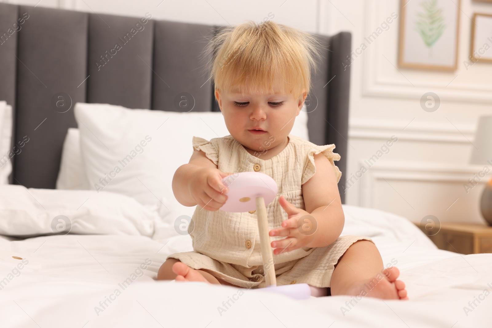 Cute baby girl in dress playing with toy on bed at home Photo of Cute baby girl in dress playing with toy on bed at home