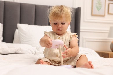 Photo of Cute baby girl in dress playing with toy on bed at home
