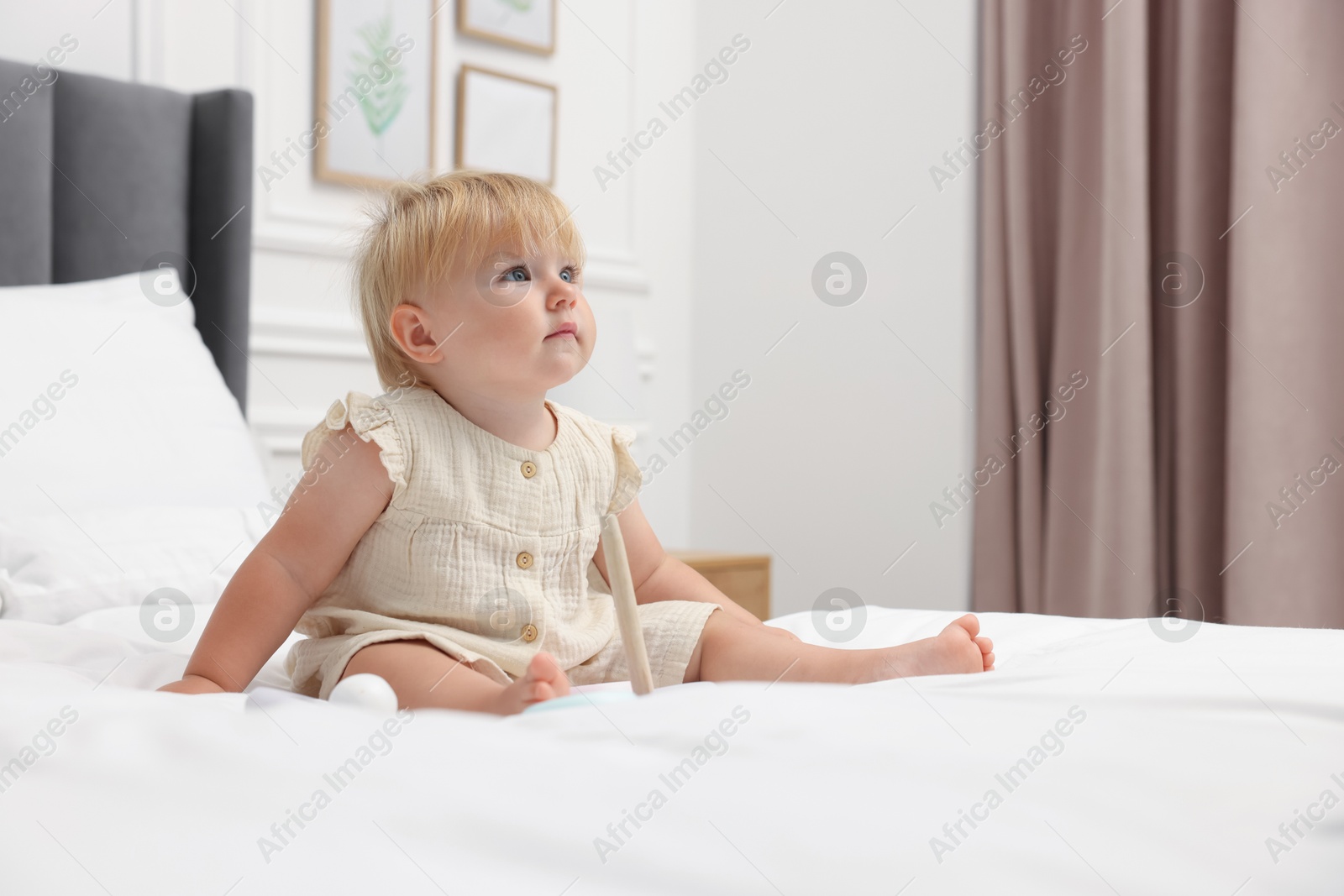 Cute baby girl in dress sitting on bed at home Photo of Cute baby girl in dress sitting on bed at home