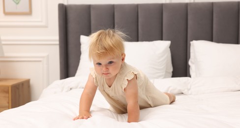 Photo of Cute baby girl in dress crawling on bed at home