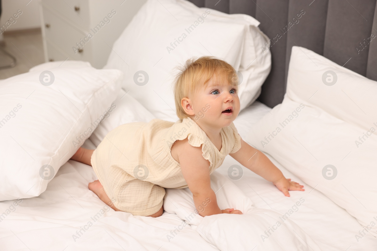 Cute baby girl in dress crawling on bed at home Photo of Cute baby girl in dress crawling on bed at home