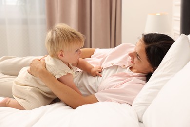 Photo of Cute baby girl and her mother on bed at home