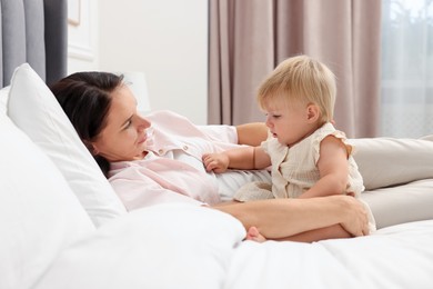 Photo of Cute baby girl and her mother on bed at home