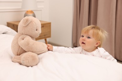 Photo of Cute baby taking toy bear from bed at home