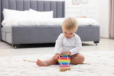 Photo of Cute baby playing with toy xylophone on floor at home