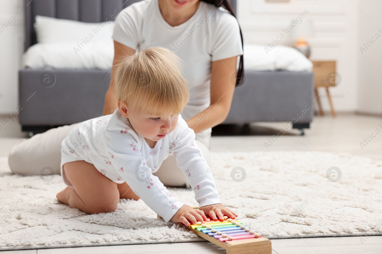 Photo of Cute baby girl and her mother playing with toy xylophone on floor in bedroom, closeup. Space for text