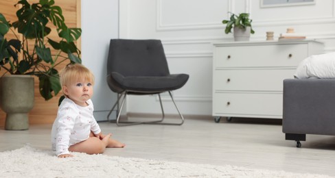 Photo of Cute baby sitting on floor at home. Space for text