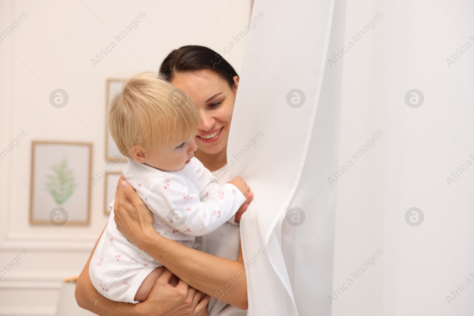 Smiling mother hugging her cute baby near curtain at home. Space for text Photo of Smiling mother hugging her cute baby near curtain at home. Space for text