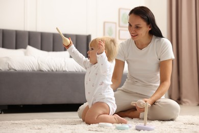 Photo of Smiling mother playing with her cute baby on floor in bedroom