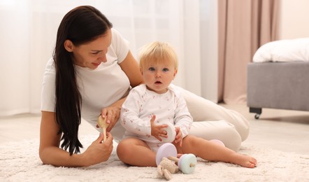 Photo of Smiling mother playing with her cute baby on floor at home