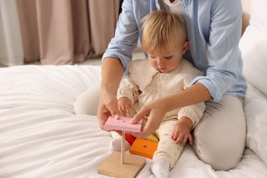Photo of Cute baby girl and her mother playing with toy on bed at home, closeup. Space for text