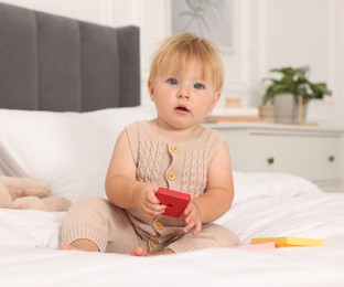Photo of Cute baby with toy sitting on bed at home