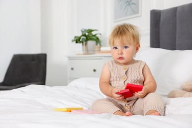 Photo of Cute baby with toy sitting on bed at home. Space for text