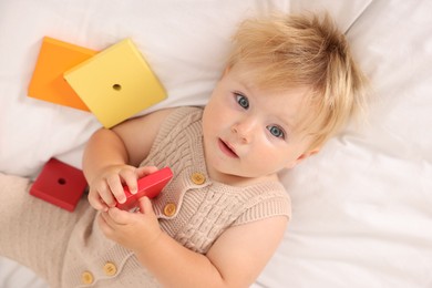 Photo of Cute baby with toys lying on white blanket, above view