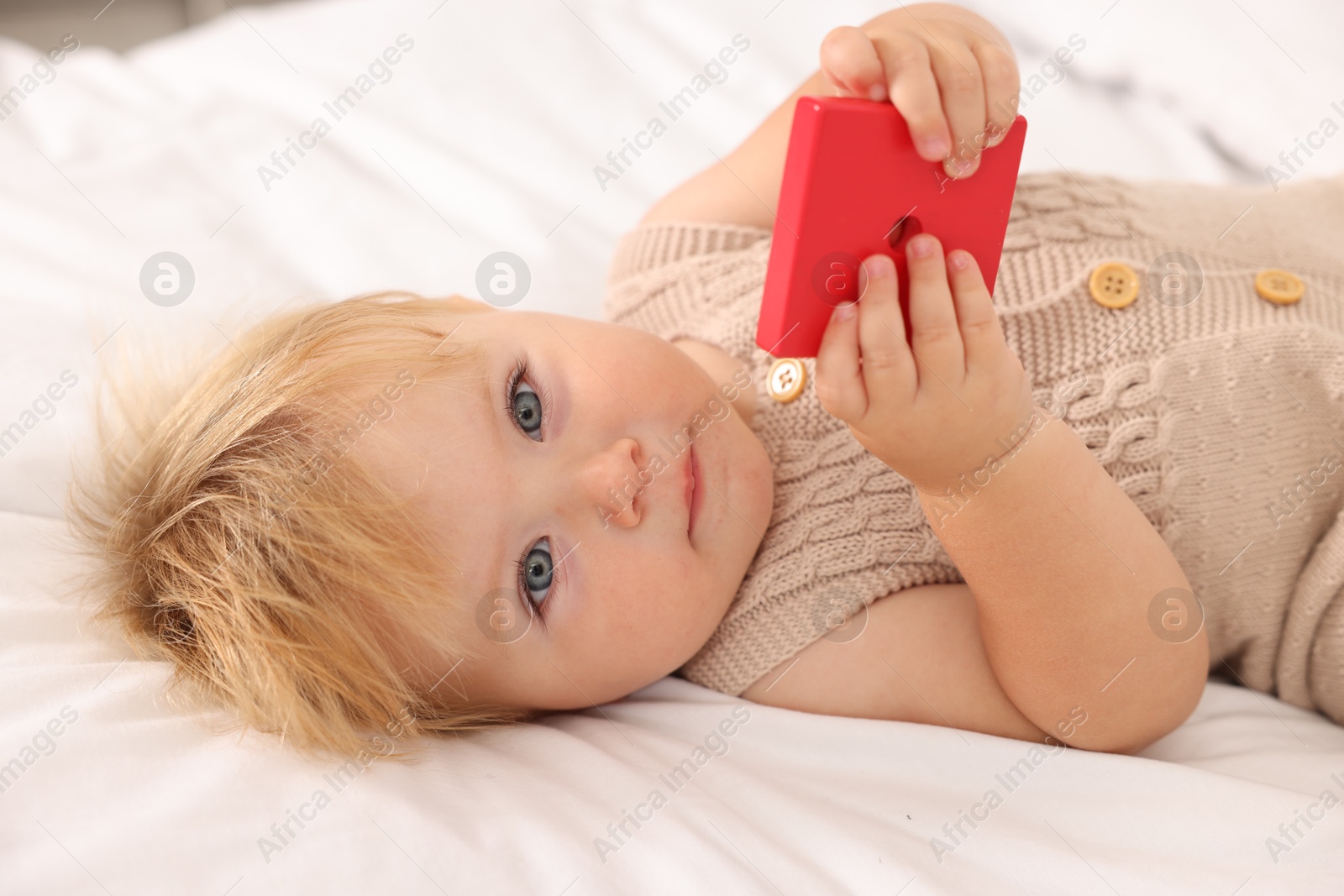 Photo of Portrait of cute baby with toy lying on white blanket, closeup