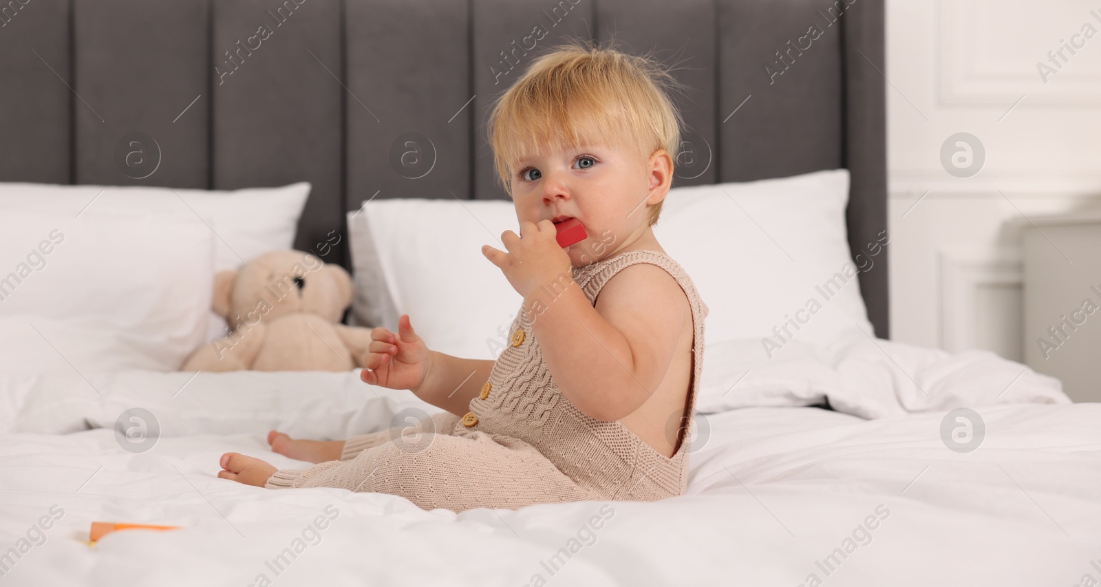 Photo of Cute baby with toy sitting on bed at home