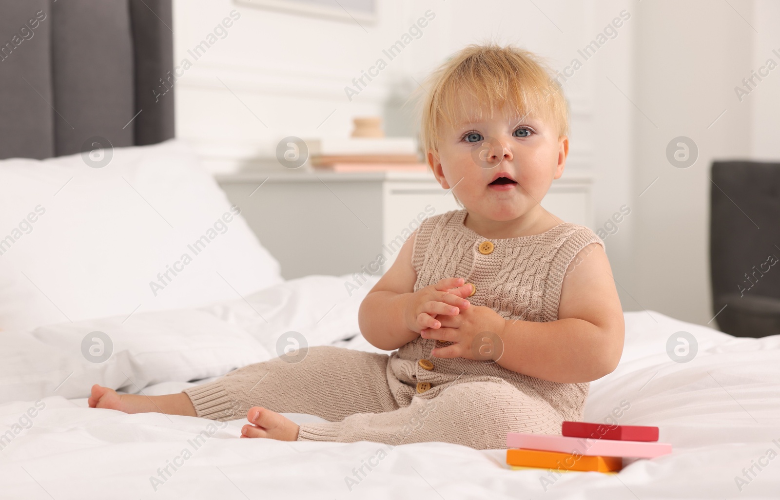 Photo of Cute baby with toy sitting on bed at home