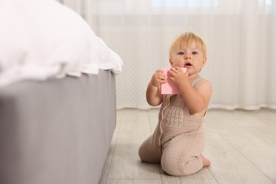 Photo of Cute baby with toy sitting on floor near bed at home
