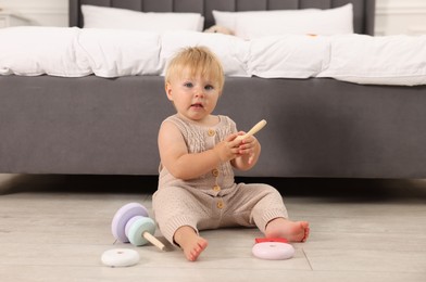 Photo of Cute baby with toy sitting on floor near bed at home