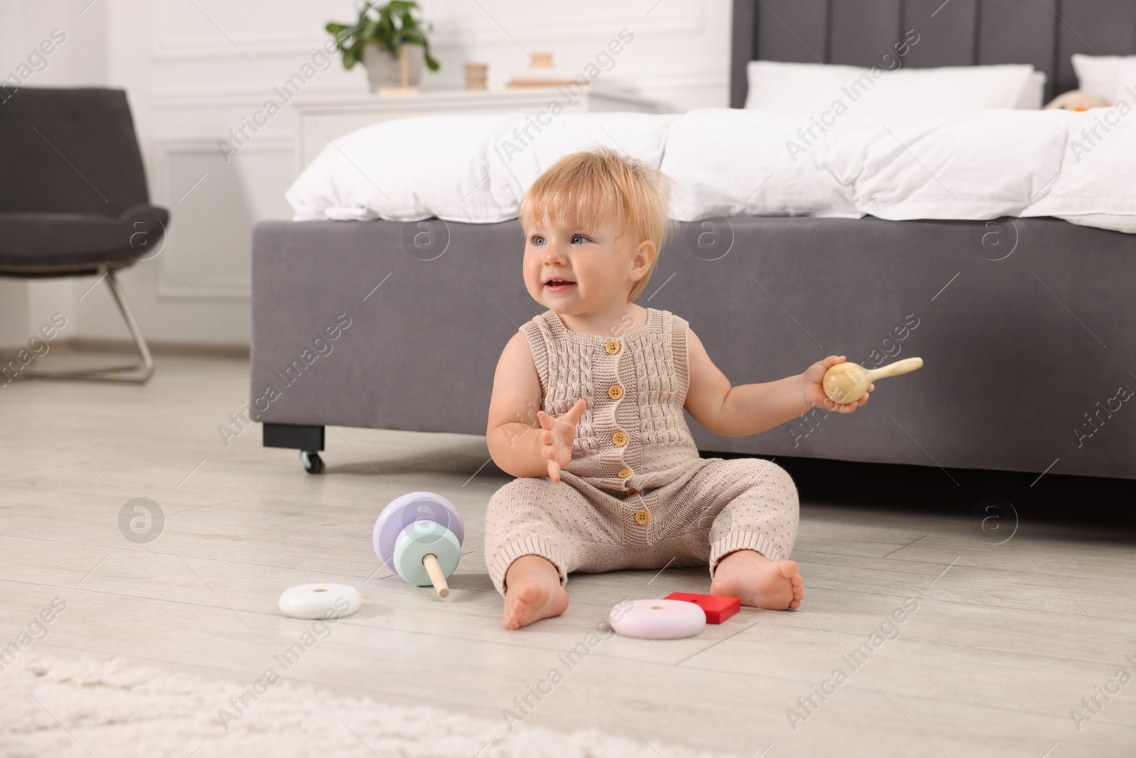 Photo of Happy baby with toy sitting on floor near bed at home