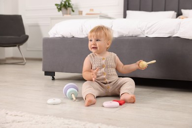 Photo of Happy baby with toy sitting on floor near bed at home