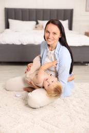 Photo of Smiling mother with her cute baby sitting on floor in bedroom