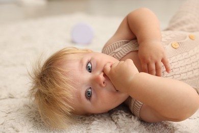Photo of Cute baby lying on beige carpet, closeup