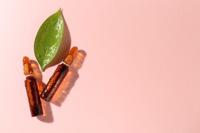 Photo of Glass ampoules with cosmetic product and green leaf on pink background, flat lay. Space for text