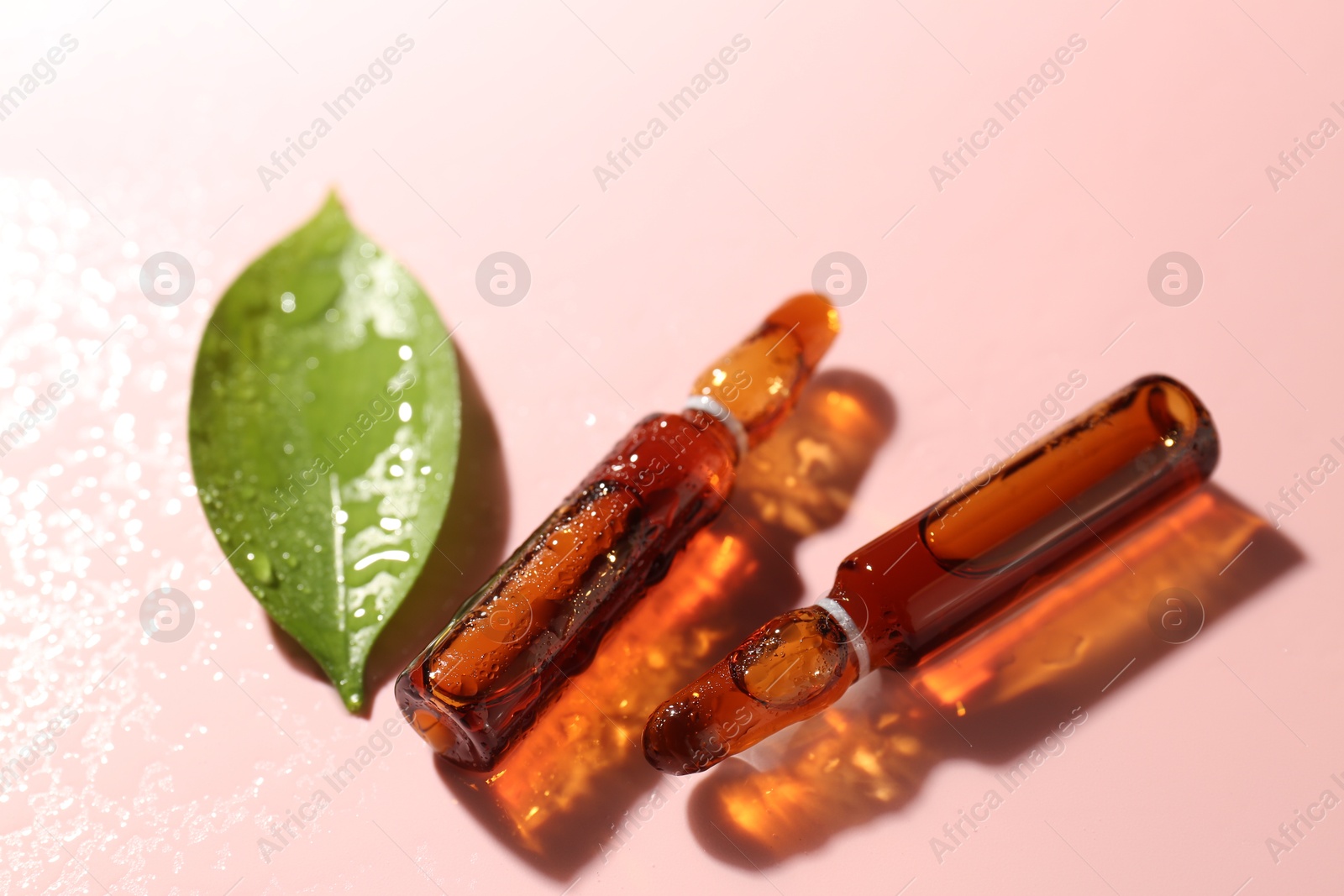 Glass ampoules with cosmetic product and green leaf on pink background, closeup Photo of Glass ampoules with cosmetic product and green leaf on pink background, closeup