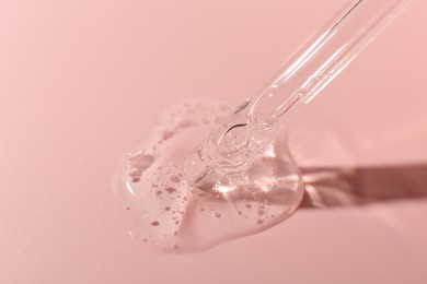 Photo of Dripping cosmetic product from pipette on pink background, closeup