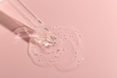 Photo of Dripping cosmetic product from pipette on pink background, closeup