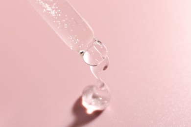 Photo of Dripping cosmetic product from pipette on pink background, closeup