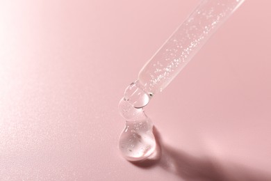 Photo of Dripping cosmetic product from pipette on pink background, closeup. Space for text