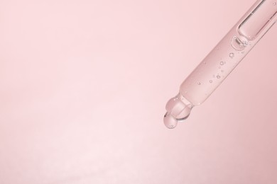 Photo of Dripping cosmetic product from pipette on pink background, closeup. Space for text