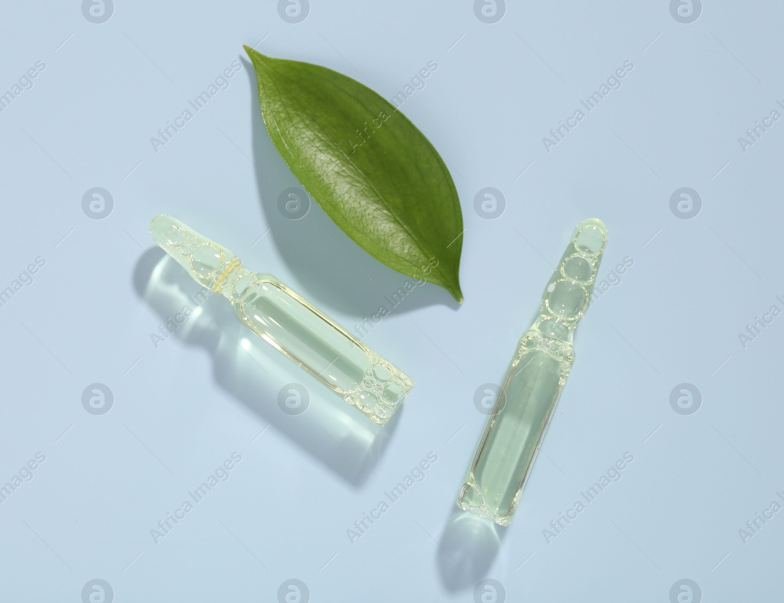 Glass ampoules with cosmetic product and green leaf on light blue background, flat lay Photo of Glass ampoules with cosmetic product and green leaf on light blue background, flat lay
