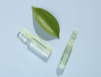 Photo of Glass ampoules with cosmetic product and green leaf on light blue background, flat lay