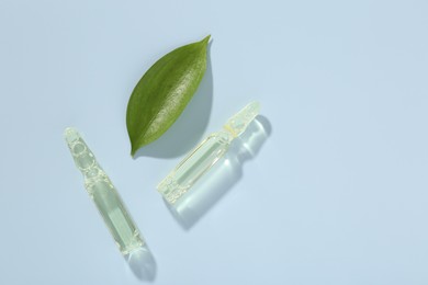 Photo of Glass ampoules with cosmetic product and green leaf on light blue background, flat lay. Space for text