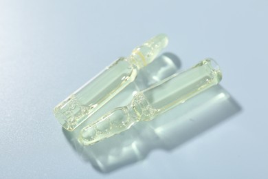 Photo of Glass ampoules with cosmetic product on light blue background, closeup