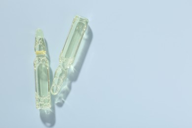 Photo of Glass ampoules with cosmetic product on light blue background, flat lay. Space for text