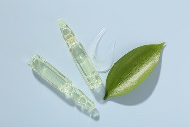 Photo of Glass ampoules with cosmetic product and green leaf on light blue background, flat lay