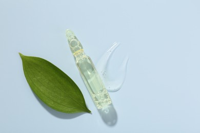 Photo of Glass ampoule with cosmetic product and green leaf on light blue background, flat lay. Space for text