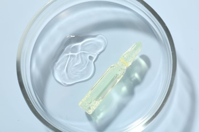 Photo of Glass ampoule with cosmetic product and Petri dish on light blue background, top view