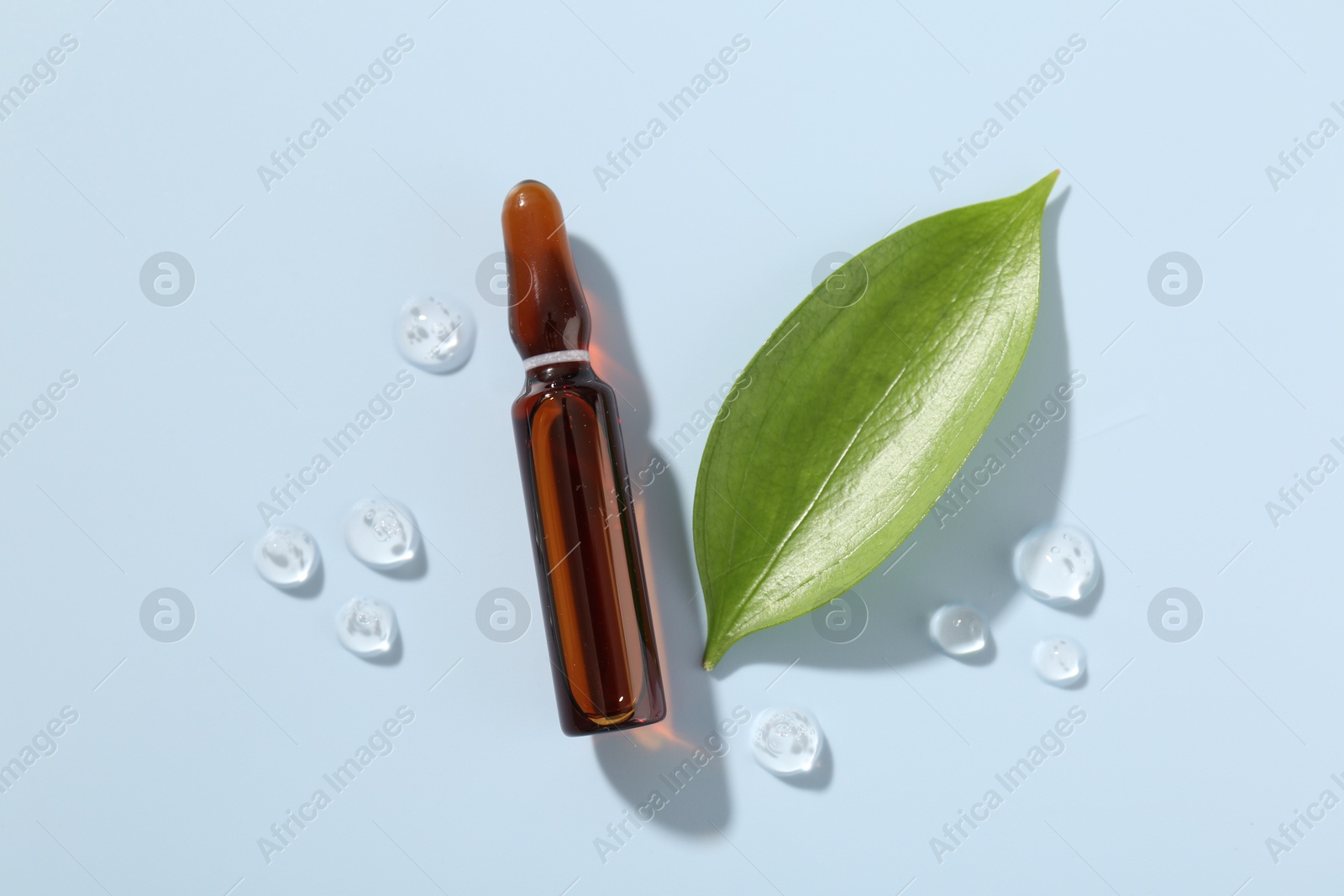 Glass ampoule with cosmetic product and green leaf on light blue background, flat lay Photo of Glass ampoule with cosmetic product and green leaf on light blue background, flat lay